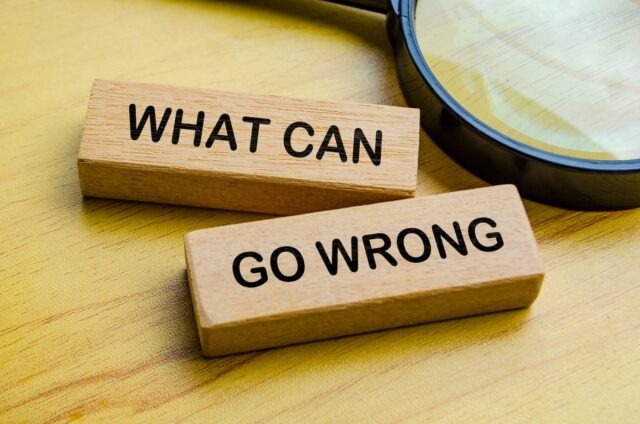 Wooden blocks displaying the words “What Can Go Wrong” beside a magnifying glass.