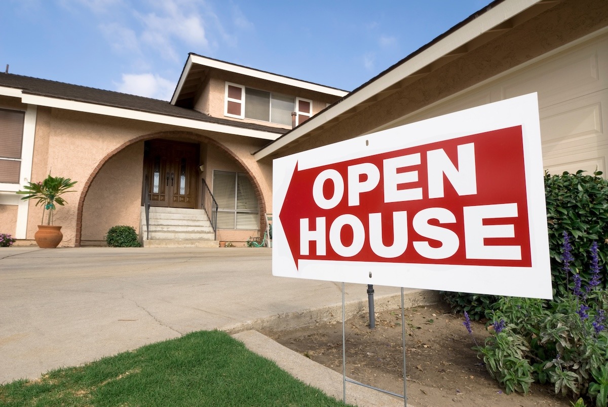 An open house sign displayed on the lawn in front of a residential home.