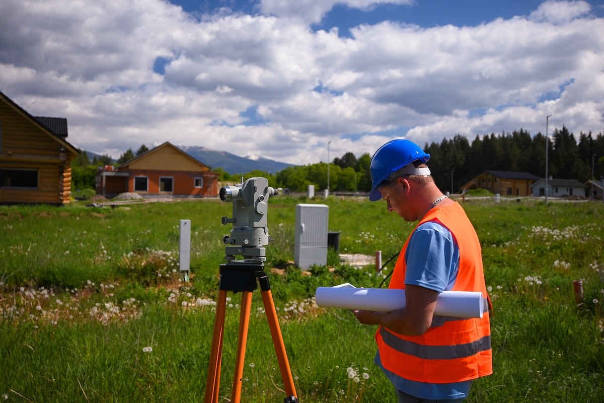 A surveyor using surveying equipment on a residential property.