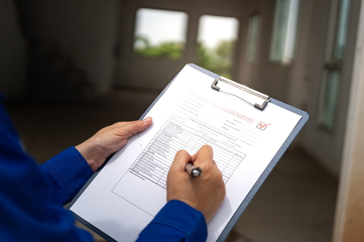 A person standing in a room holding a clipboard with an inspection form and writing on it with a pen.
