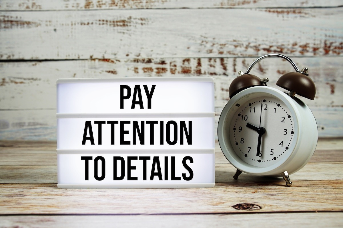 An alarm clock beside a light box displaying the words “Pay Attention to Details.” 