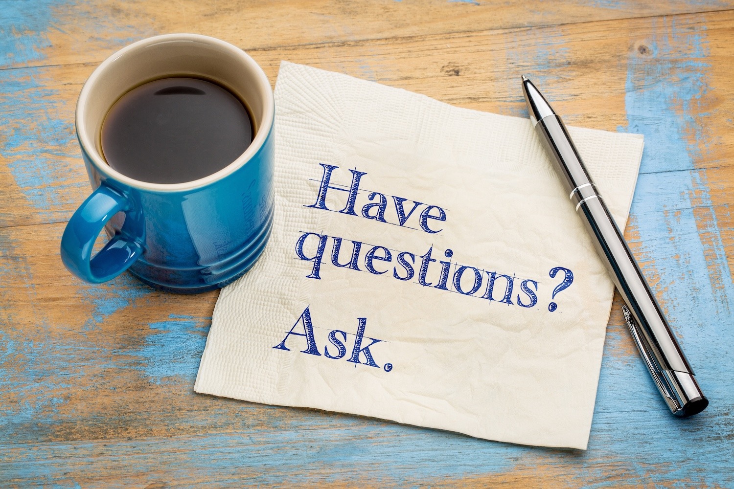 Coffee cup beside a napkin with the message “Have questions? Ask.”