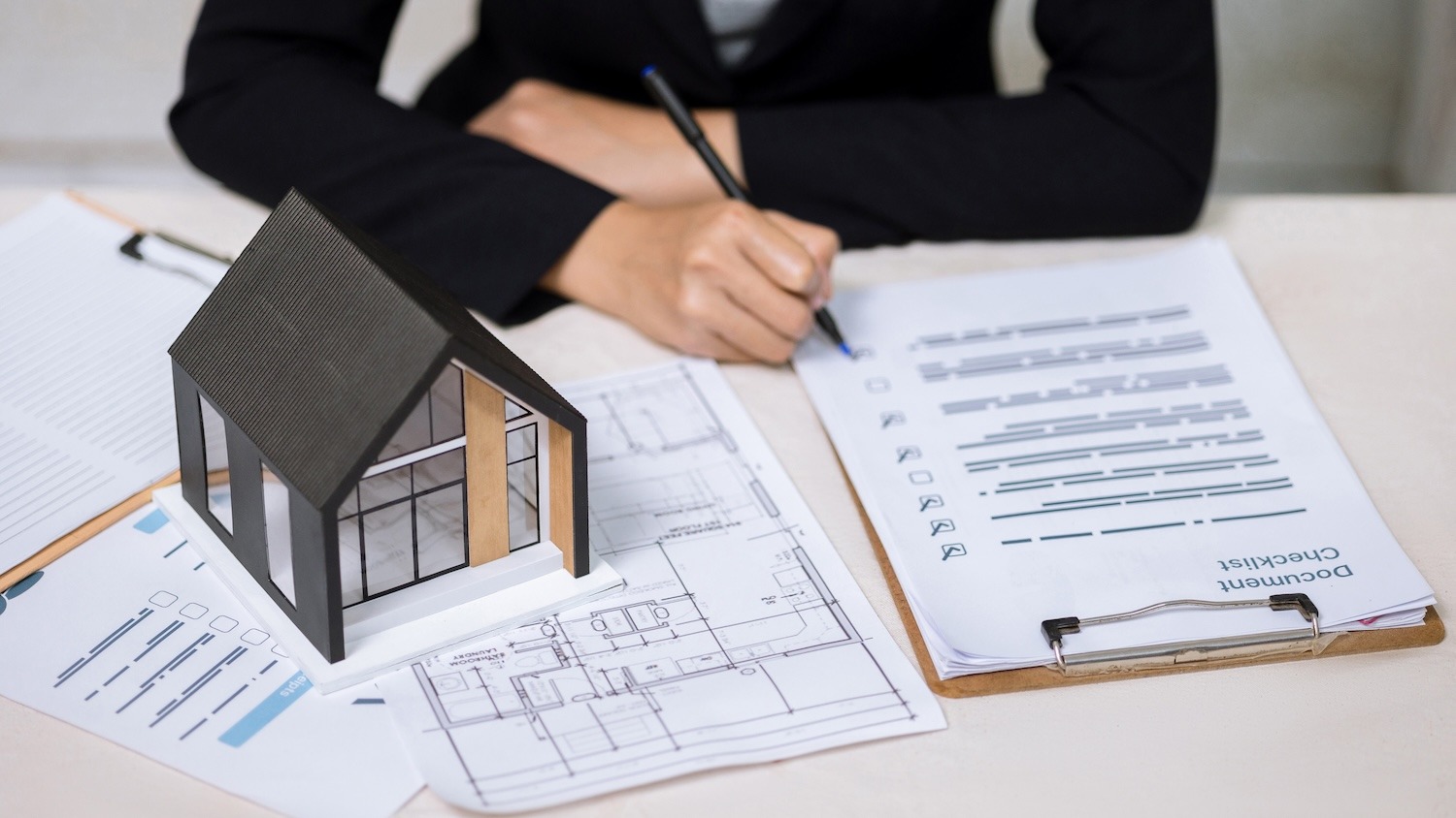 Professional reviewing property plans and a checklist beside a model house.