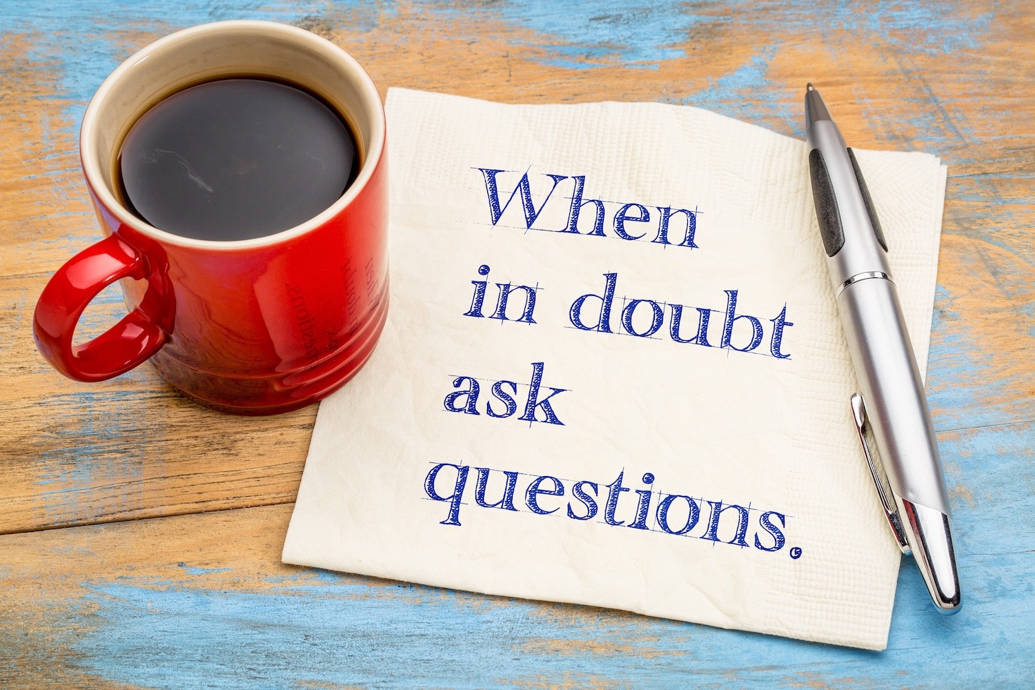 Coffee cup beside a napkin with the message “When in doubt ask questions.”