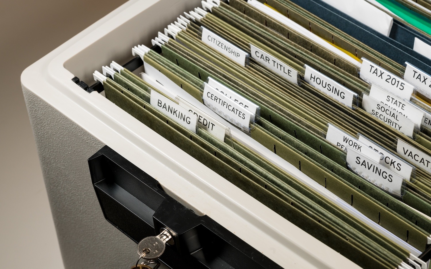 Organized hanging file folders labelled with financial and personal record categories beside a key