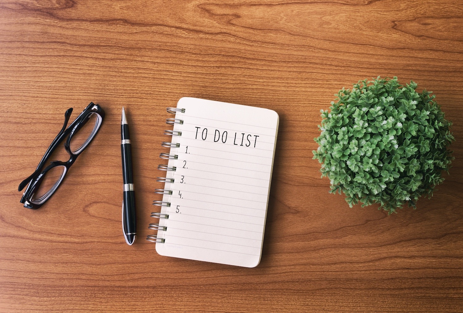 Blank to-do list notebook with glasses and pen on a wooden desk