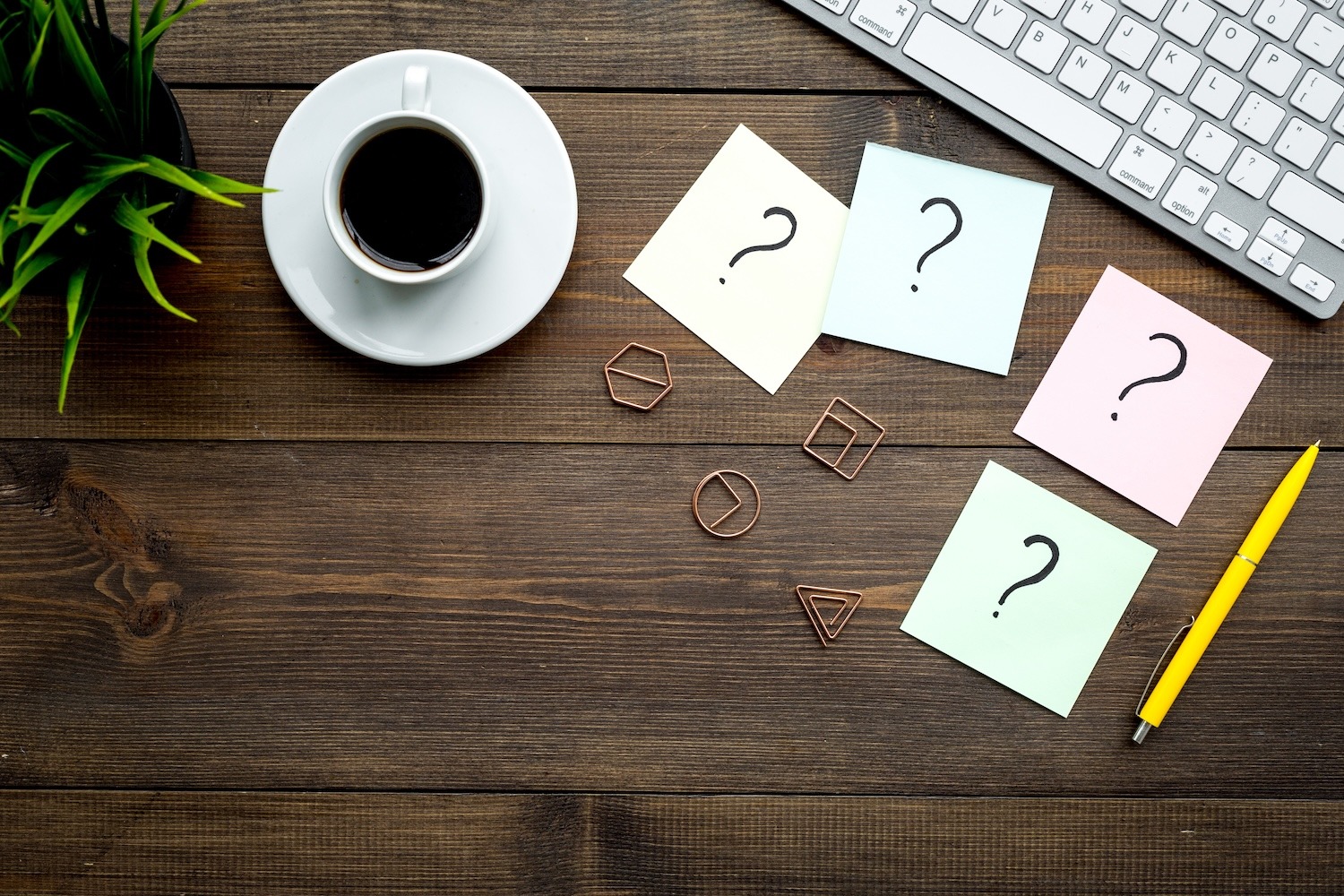 Colourful sticky notes with question marks beside a keyboard and coffee cup