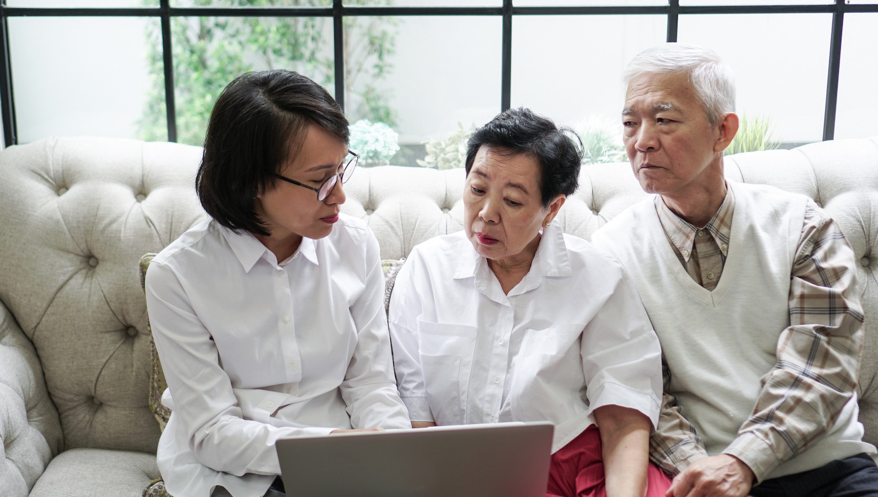 First Time Executor. Asian senior couple discuss their wills with their executor on their coach in there home.