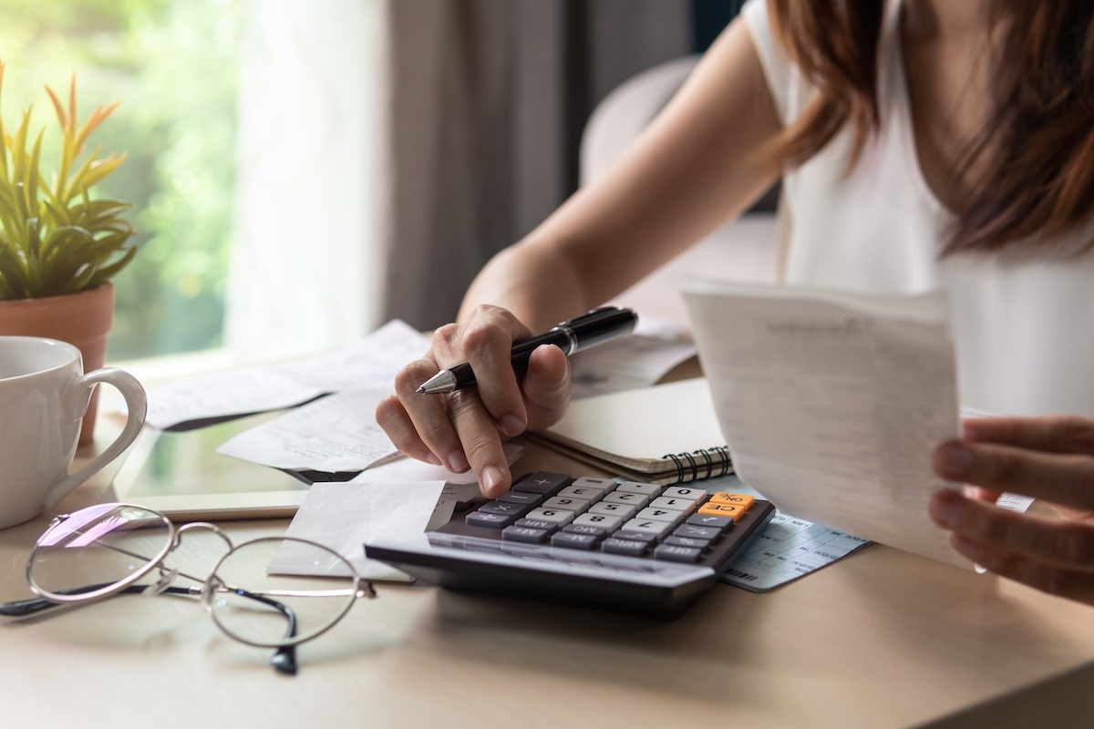 A person at a desk using a calculator with one hand while holding a receipt in the other hand.