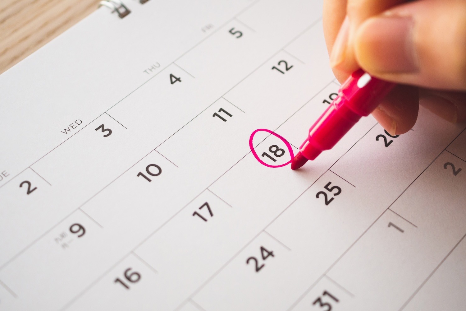 Hand circling a date on a calendar with a pen