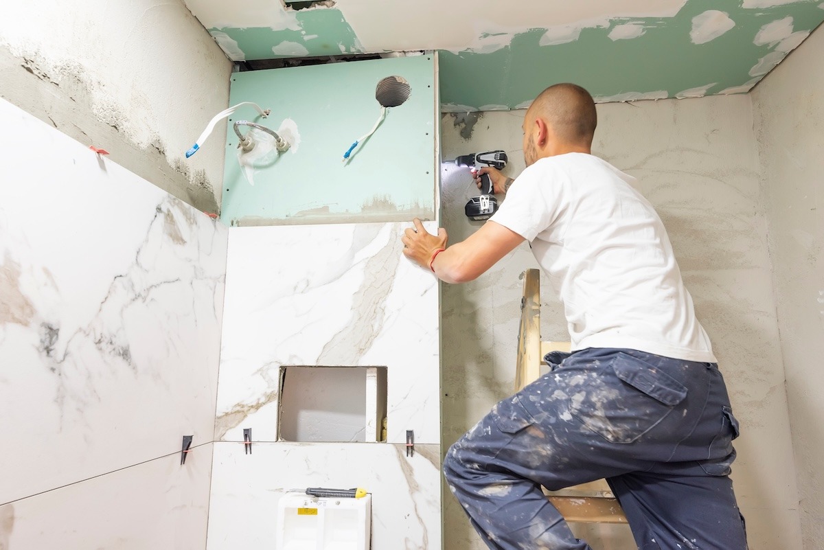 A worker repairing a bathroom ceiling and walls with visible drywall work in progress.