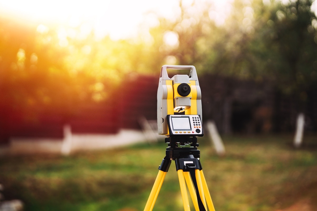 Professional land surveying equipment on a tripod being used to measure property and land features.