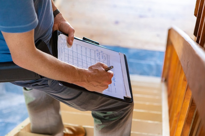 Home inspection. A close up and high angle view of a professional male wearing blue t-shirt, writing out forms during a home inspection, standing on stairs.