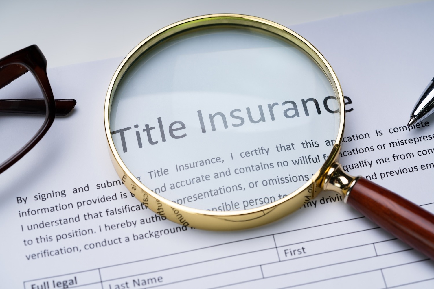 Magnifying glass over a title insurance document with eyeglasses and a pen.
