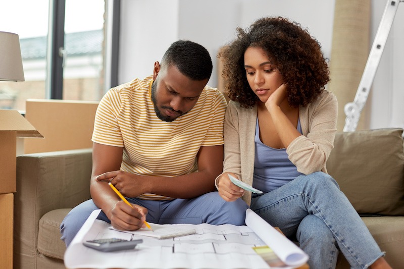 Home purchase preparation. Mortgage, moving and real estate planning. Serious couple of colour with blueprint and calculator counting estimating repair costs to next home