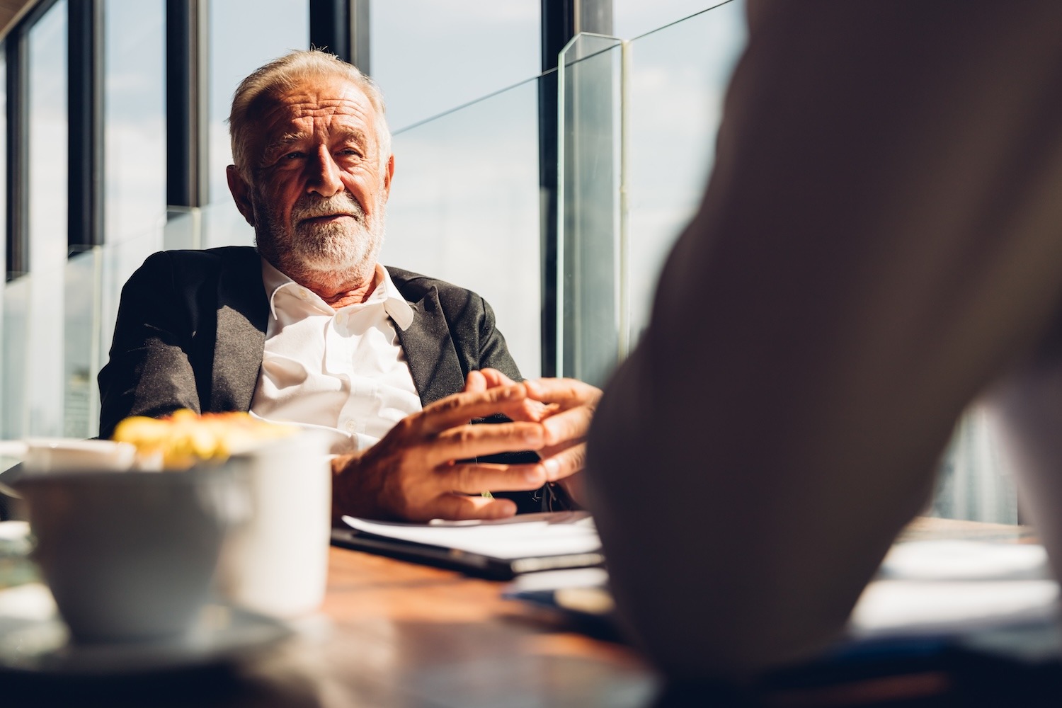 Older man speaking with another person across a table during a casual conversation