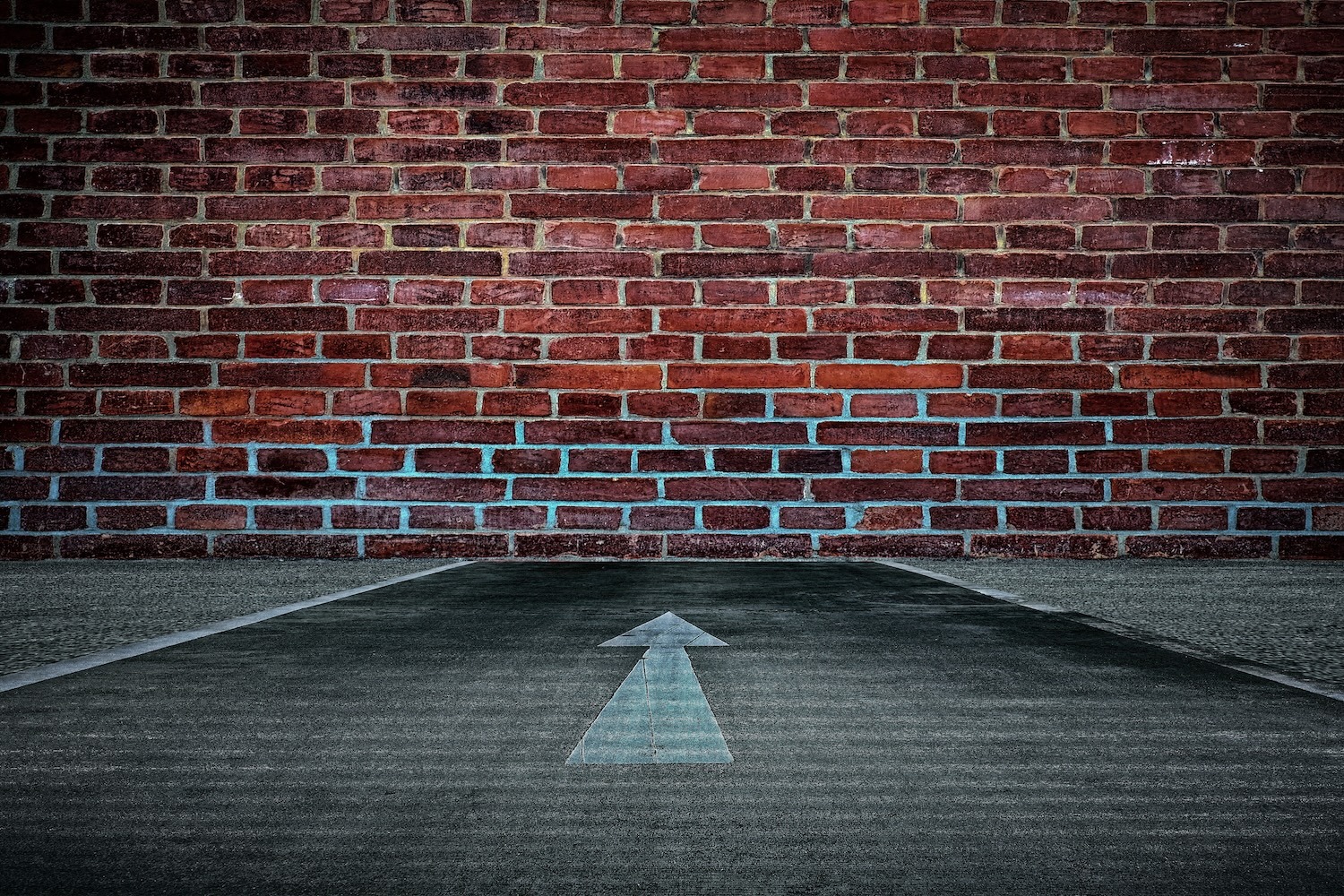 Directional arrow on pavement pointing toward a brick wall