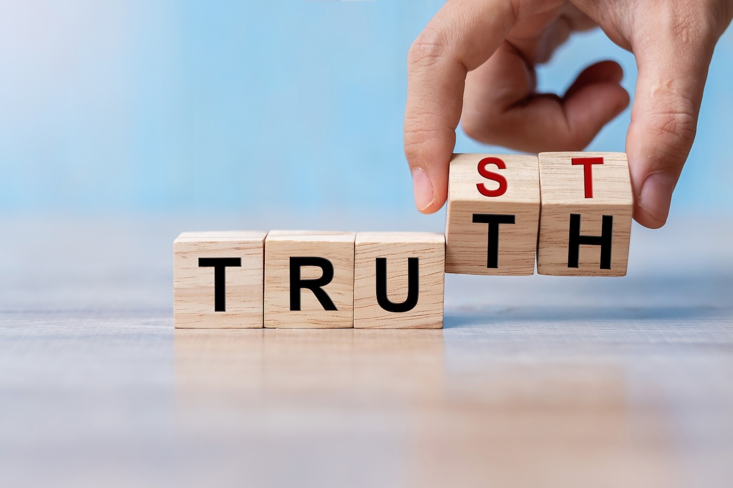 Hand arranging wooden letter blocks to complete the word “TRUTH.”