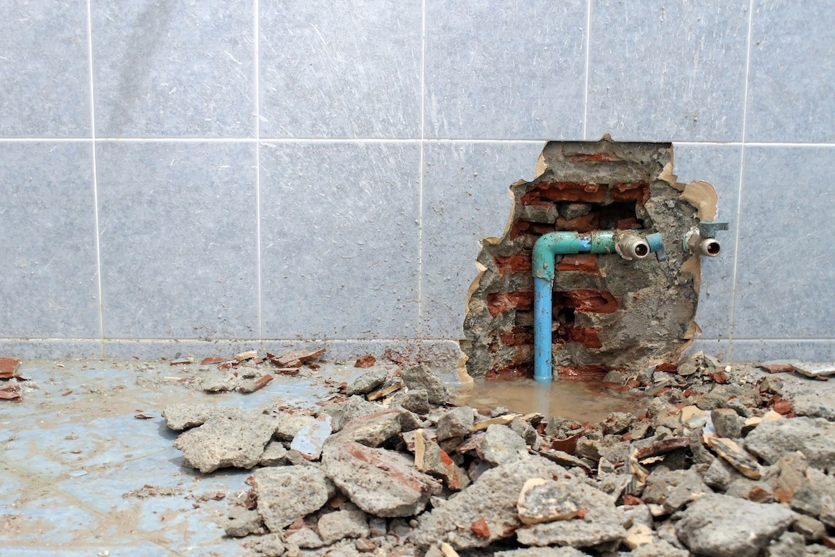 Damaged interior wall with exposed plumbing pipes and construction debris during a major home repair.