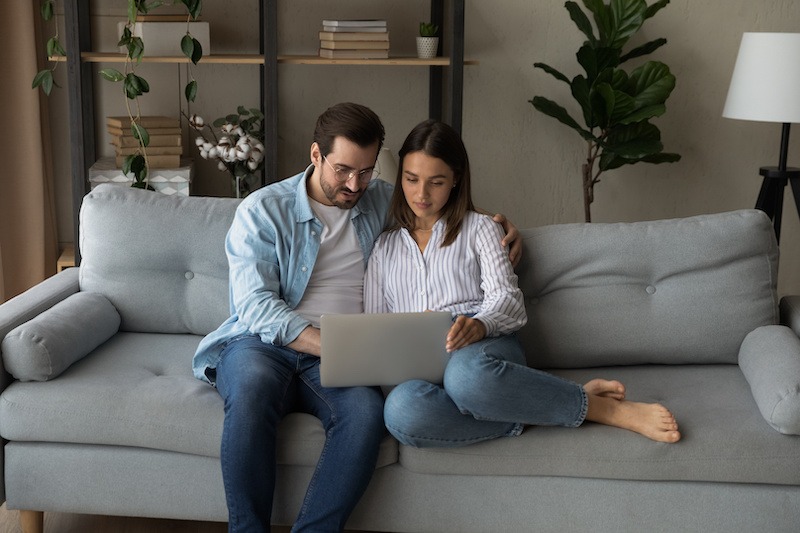 Next home purchase. Serious young couple sit on sofa by laptop home purchase planning. Surf the internet together searching for new house to buy.
