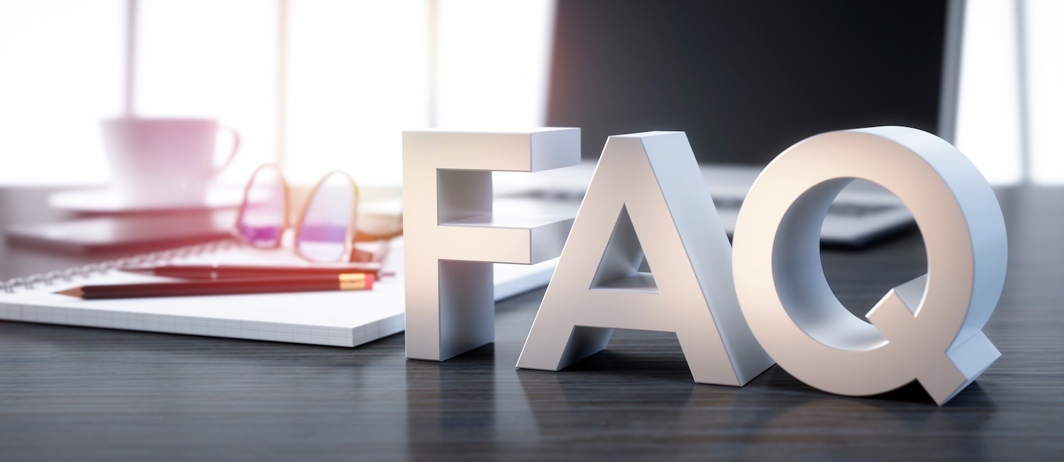 Three-dimensional FAQ letters on a desk beside a notebook, eyeglasses, and computer.