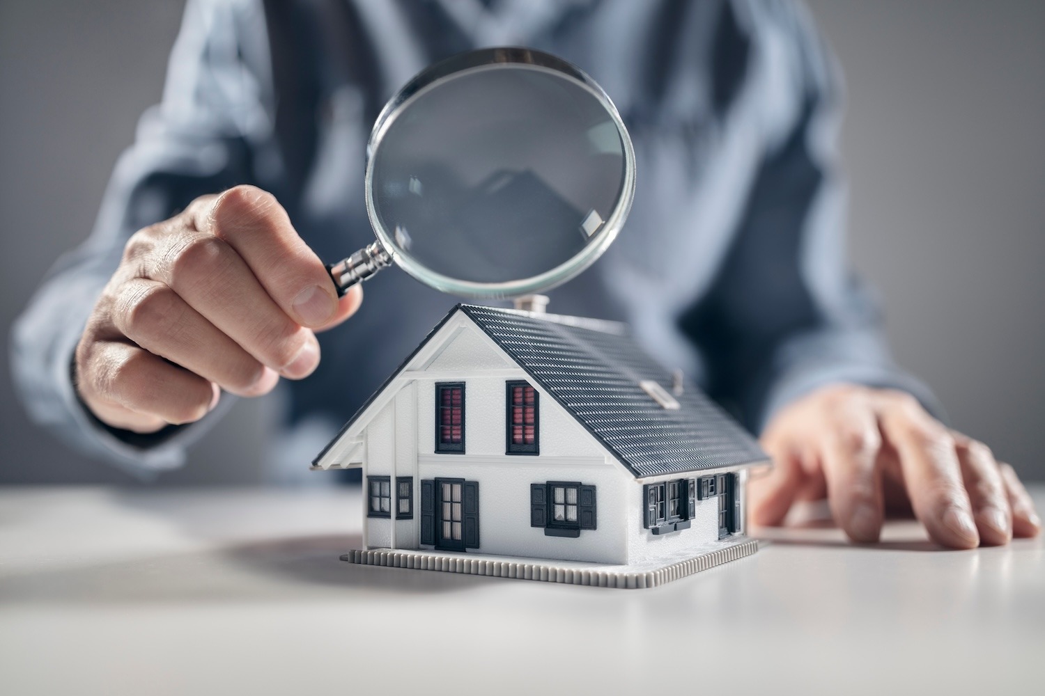 Magnifying glass positioned over a model house to represent examining a home more closely.