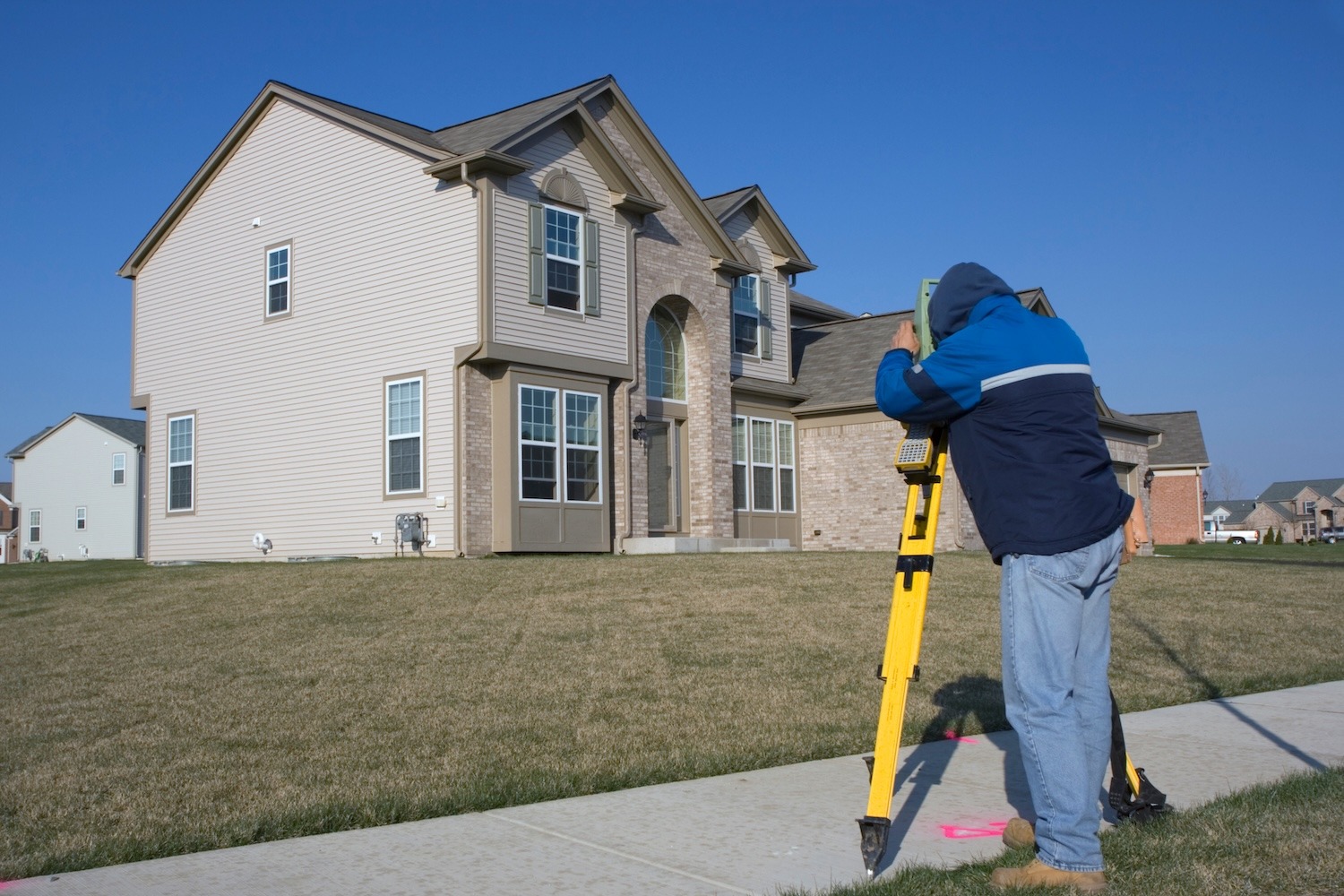 Land surveyor using a total station to measure a residential property.