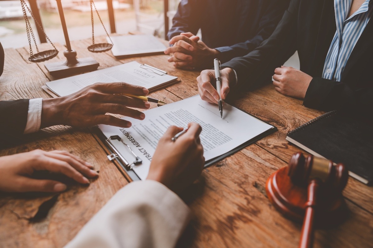A close-up of several people at a desk reviewing a contract, with one person pointing to details on the agreement.