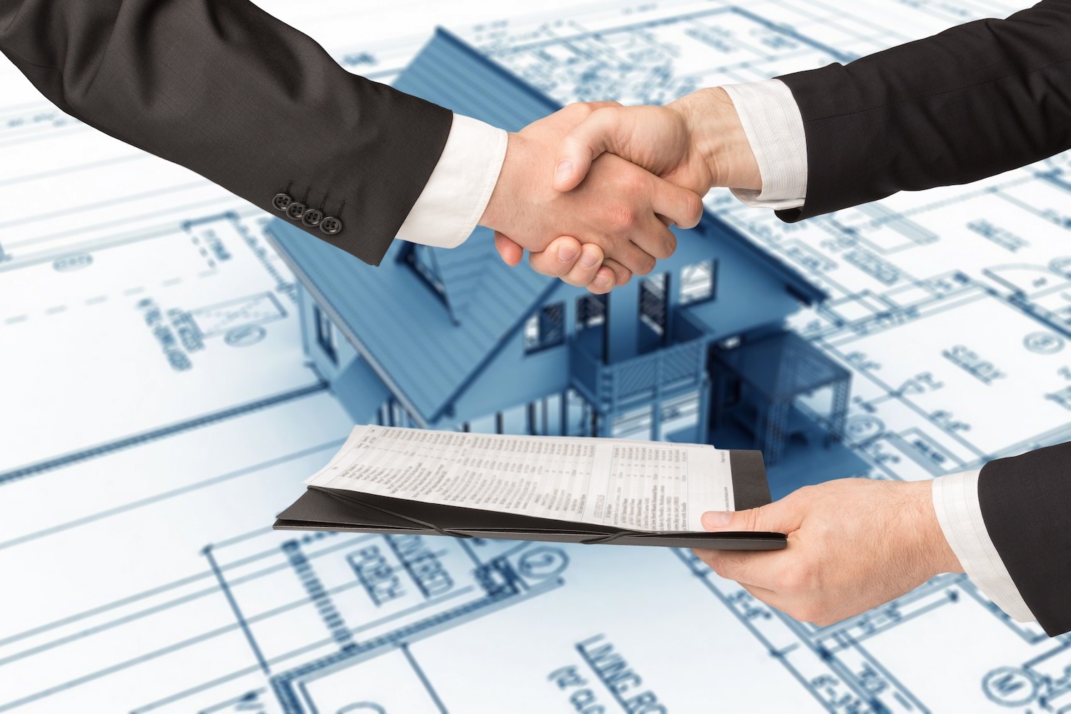 Two people shaking hands over residential property plans and a model house.