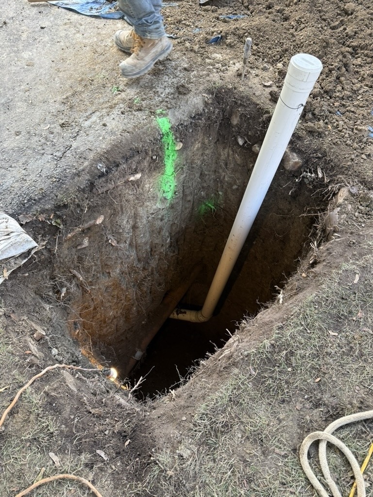 Deep excavation in a residential front yard to access and repair an underground sanitary drain line.